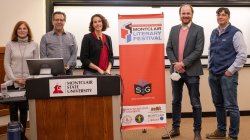Five people pose for a photo near a podium and Montclair Literary Festival sign.