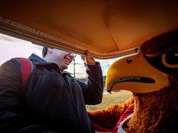 A male student helps a school mascot into a golf cart.