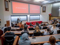 A woman speaks in front of a classroom full of students.