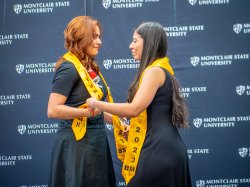 Two sisters, wearing yellow graduation stoles, face one another, holding hands and crying as they celebrate becoming nurses.