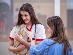 A female student holds a bunny while another pets it.