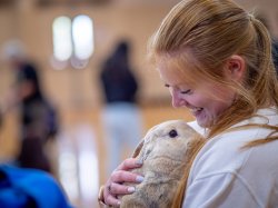 A student smiles as she snuggles a rabbit.