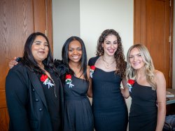 Four nursing students pose together wearing formal black clothing with red roses