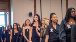 A long line of students wearing formal black clothing walk into the ceremony.