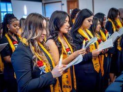 Graduates hold candles and read from a program.