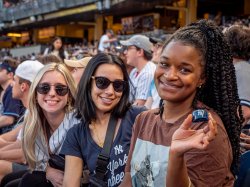 Three women, two wearing sunglasses, smile and one holds a tiny Yankees baseball cap.