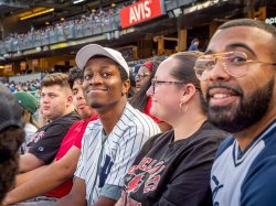 A student wearing a Yankees jersey grins at the camera as other spectators watch the game.