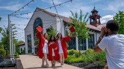 Three students in red caps and gowns pose for a photo on campus