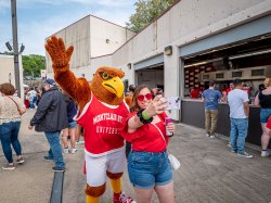 a student poses for a selfie with Rocky the Red Hawk