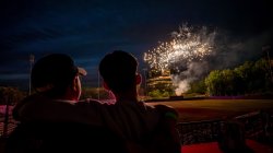 Two spectators watch fireworks exploding over a ballpark.