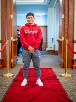 Student in a red Future College Graduate sweatshirt stands on a red carpet.