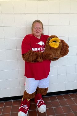 A student in a mascot costume smiles while holding the costume’s head in their arms.