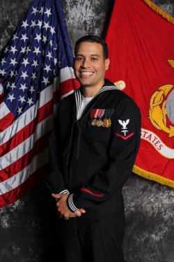 A man in uniform stands between the U.S. and Navy flags.