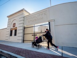A woman pushes a baby carriage past the gates to a baseball stadium.