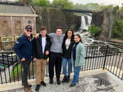 A professor and four students stand in front of a waterfall.