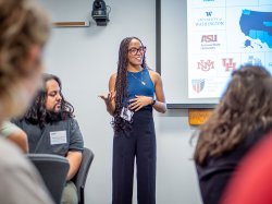 A young woman stands at the front of a room, addressing students.