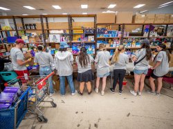 Eight students stand with backs to the camera as they work at a food pantry.