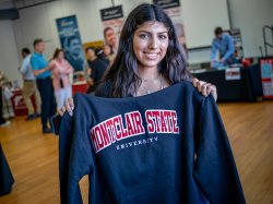 A smiling female student holds up a Montclair State University sweatshirt.