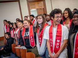 Students, standing and smiling, wear red stoles with letters EOF and MSU.