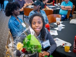 A student holds a bouquet of roses while seated at a table.