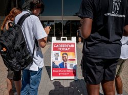 Students look at their phones in front of a sign advertising a career fair that has a QR code on it.