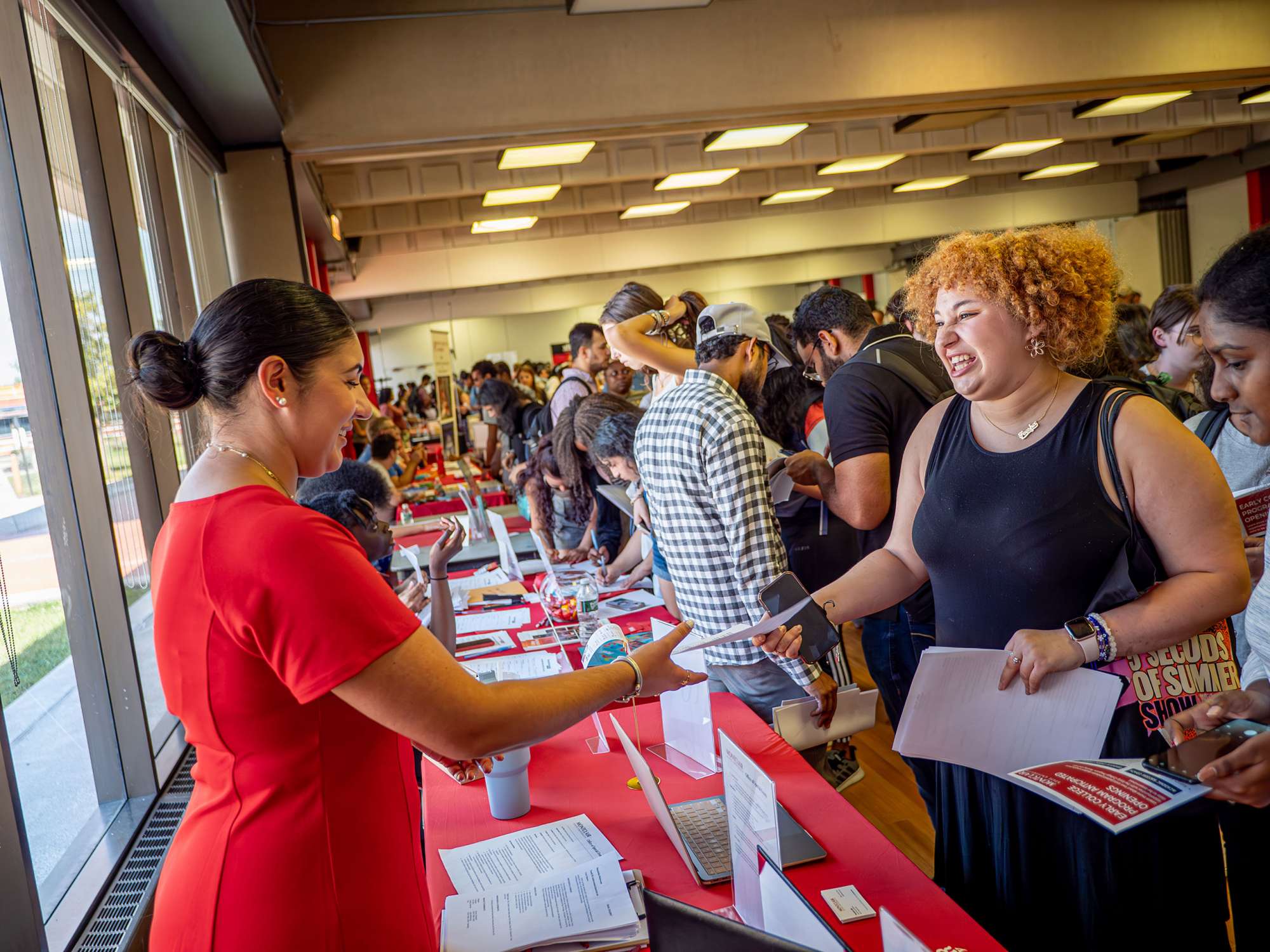 A student holds out a sheet of paper to a woman across a table.