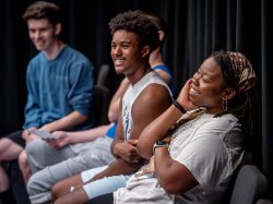 An acting teacher smiles while seated with two students.