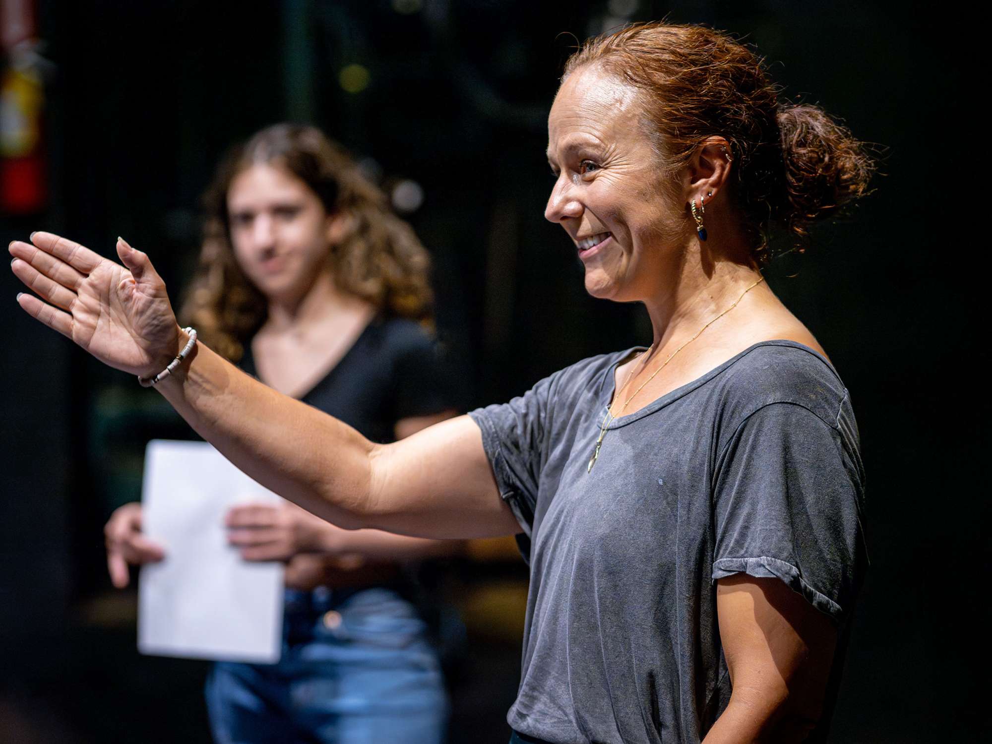 An smiling acting teacher gestures to students.