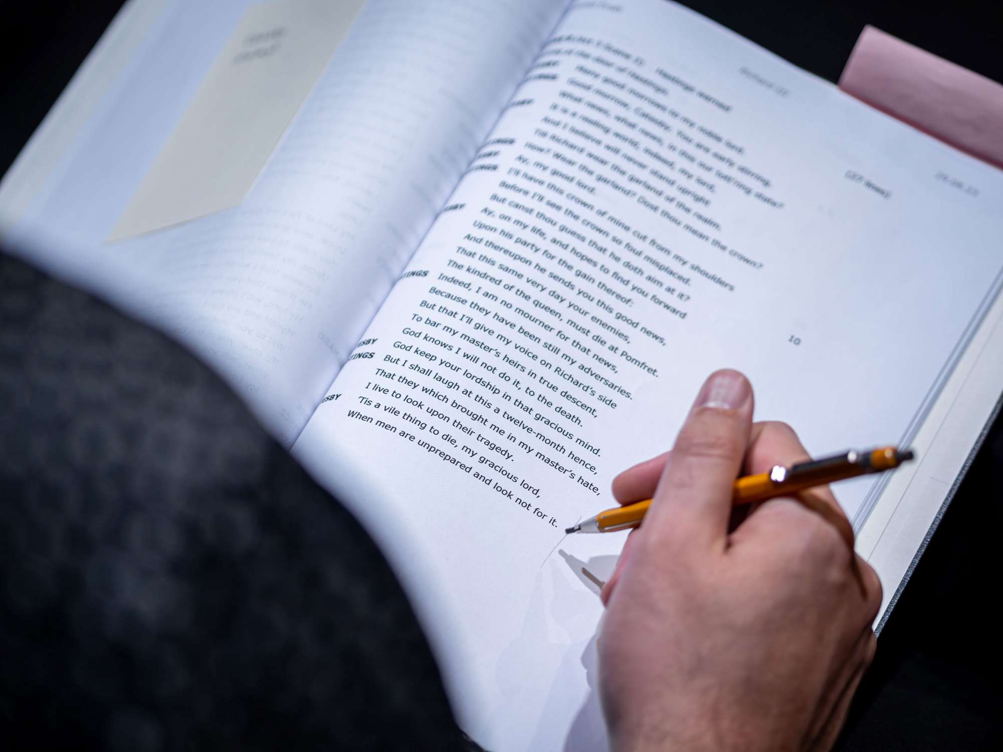 A hand with a pencil, follow along on a page from a Shakespeare play script.