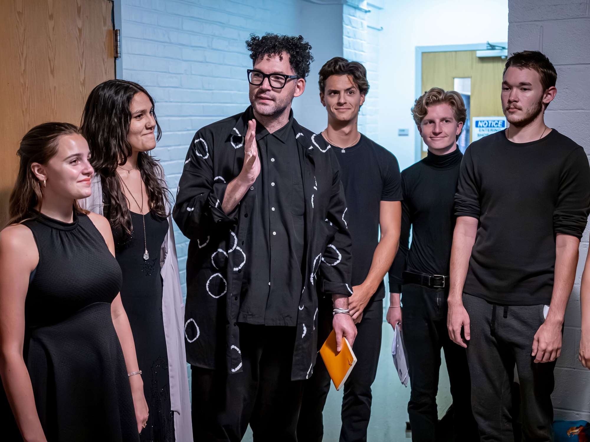 The play’s director stands in the center of five students, all dressed in black.