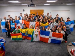 A large group of students, faculty and staff pose with flags from Latin American countries.