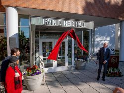 Three people pull down a cover to reveal the Irvin D. Reid Hall sign