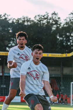 Two soccer players celebrate by pumping their fists after scoring a goal.