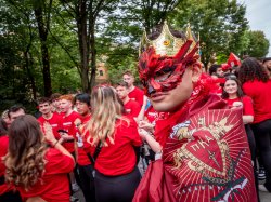 A man dressed in a crown and red feather eye mask and a fraternity flag .