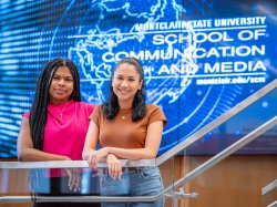 Two students stand before a Montclair State University School of Communication and Media screen.