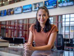 A student sits at a news desk in front of multiple TV screens in Montclair’s News Lab.