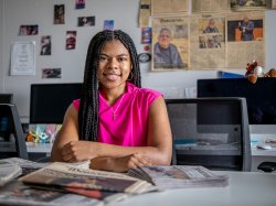 A student sits at a desk surrounded by newspapers.