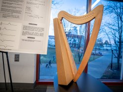 A harp against a window with a view of campus behind it.