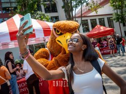 A woman poses for a selfie with a mascot.