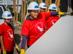 Students wearing hardhats and red Montclair shirts with the words "Soaring into Service" work at a construction site.