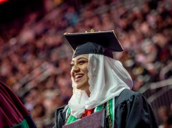 a smiling graduate wearing a hijab with cap and gown