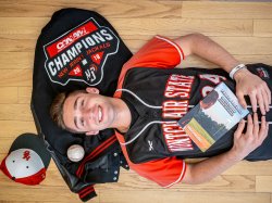 Billy Pinckney rests on his back on his baseball jacket and holds his book.