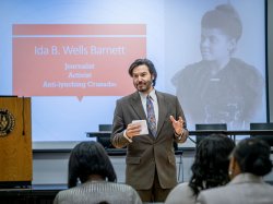 A man stands in front of a screen with a photo of a woman and the words Ida B. Wells Barnett, journalist, activist and anti-lynching crusader.