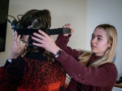A female student straps virtual reality goggles onto another student.