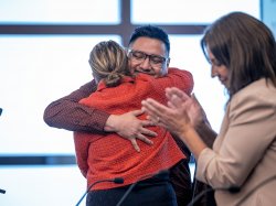 A woman hugs a man as a woman claps nearby.