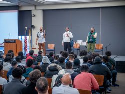 Three men perform a spoken word piece onstage for an audience of young male students.