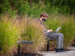 Male sitting outside on a bench, wearing a mask