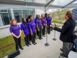 A school choir, wearing purple shirts, sings.