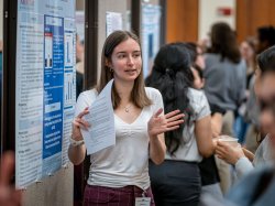 A student gestures as she discusses her research poster.