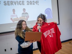 Student Mariana Luna-Martinez holds a computer as Bonner Leader and Service Coordinator Mikaela Guzman looks on while holding a Montclair sweatshirt.